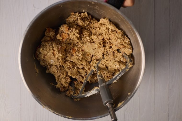 Oatmeal cookie dough with apple pieces and cinnamon chips in a stand mixer bowl.