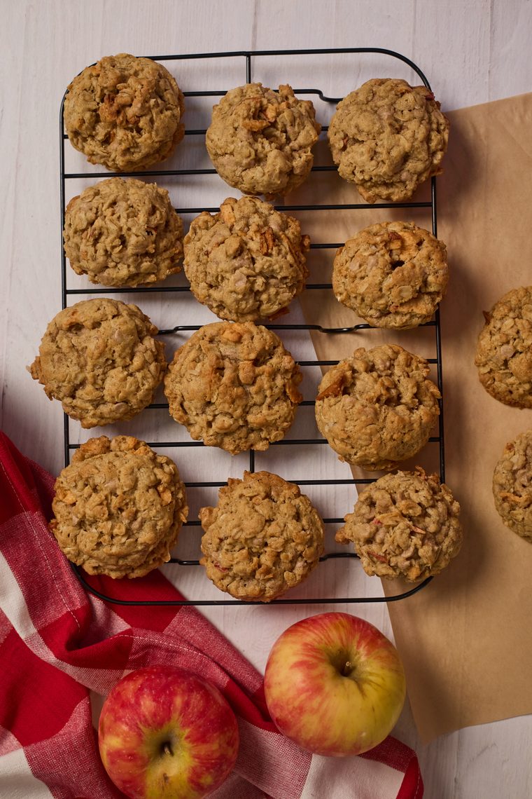 Oatmeal apple cinnamon cookies cooling on a wire rack beside apples.
