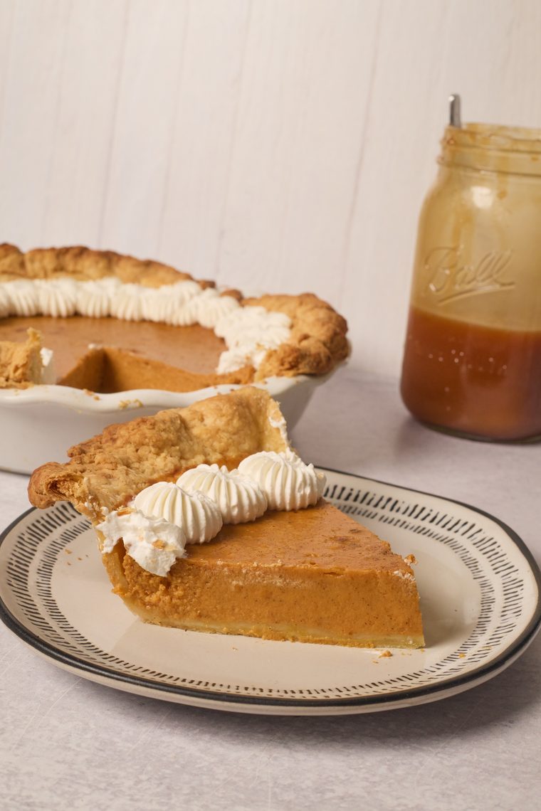 A slice of pumpkin pie topped with piped whipped cream on a patterned plate.