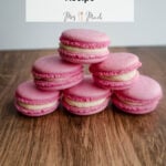 A stack of pink macarons with creamy filling sits on a wooden table. Above them, the text says: Easy Swiss Macarons Recipe.