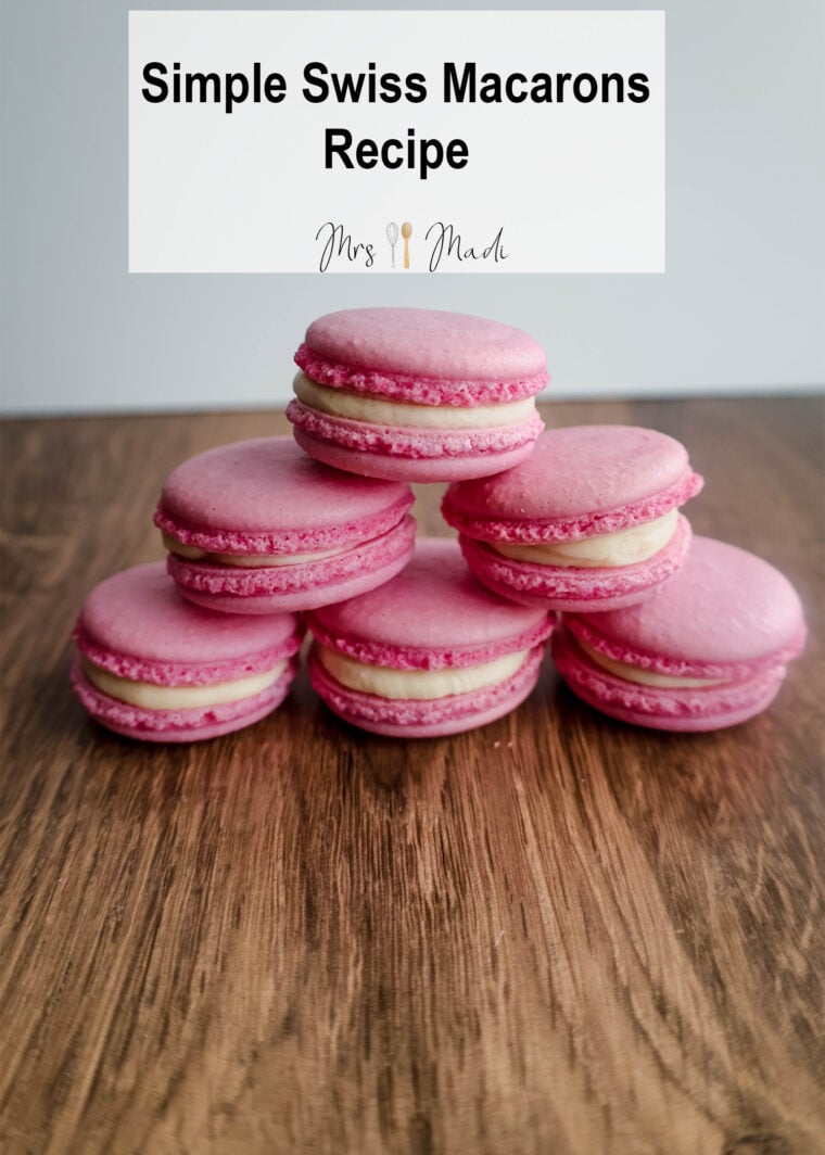 A stack of pink macarons with creamy filling sits on a wooden table. Above them, the text says: Easy Swiss Macarons Recipe.