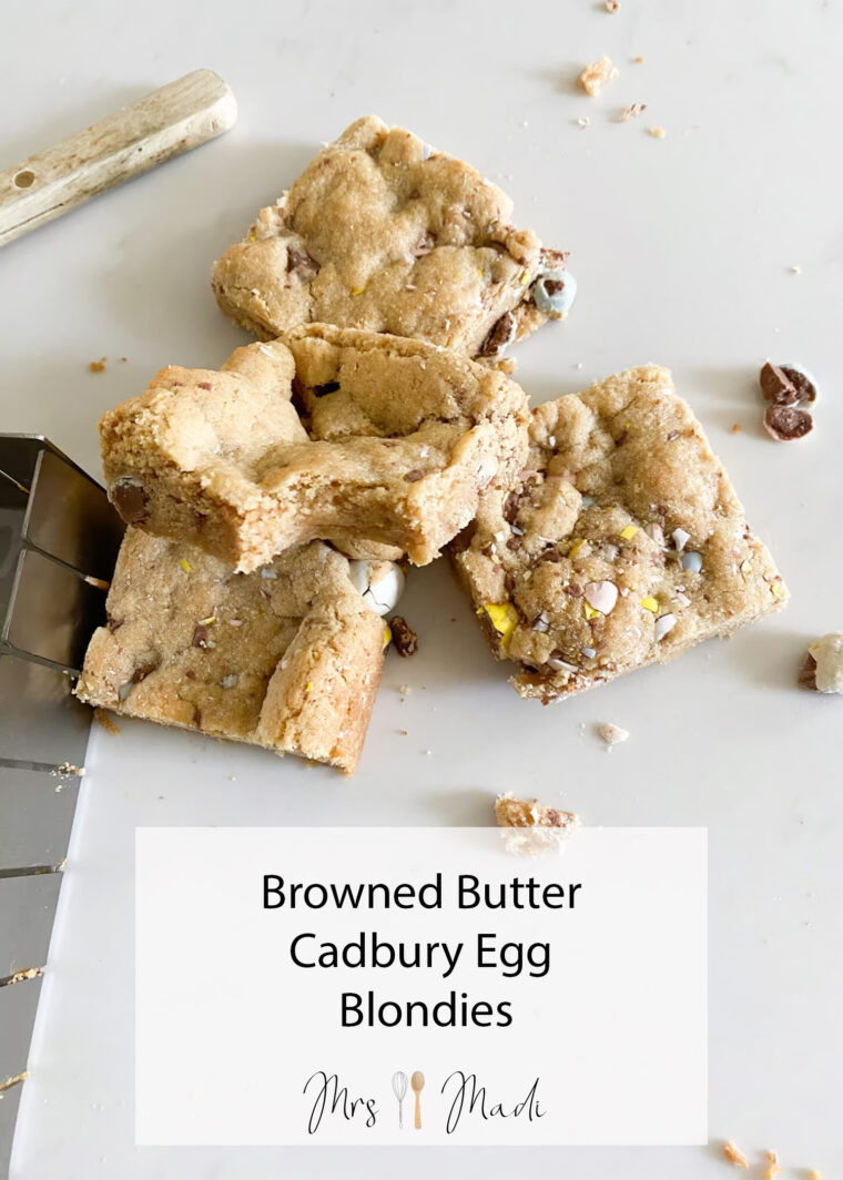 A stack of browned butter Cadbury egg blondies sits on a white surface, spatula and crumbs making it look extra tasty.