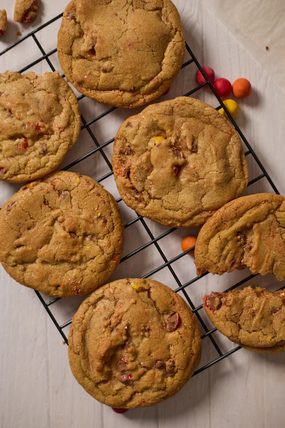 Browned butter Cadbury egg cookies cooling on a wire rack beside colorful chocolate eggs.