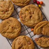 Browned butter Cadbury egg cookies cooling on a wire rack beside colorful chocolate eggs.
