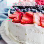 A white-frosted tres leches cake loaded with fresh strawberries, blueberries, and blackberries sits on a white plate. Up top, it says: “Cinnamon Tres Leches Cake Recipe.” There’s a blue cloth in the background.