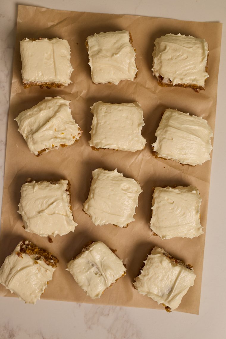Overhead view of cream cheese frosted pumpkin bars arranged on parchment.