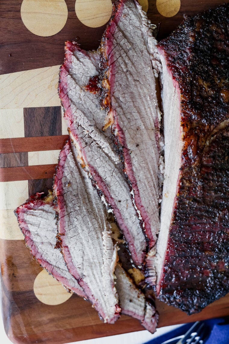 Tender smoked brisket with a dark crust and pink smoke ring, sliced up and laid out on a cool wooden cutting board—looks seriously tasty!.