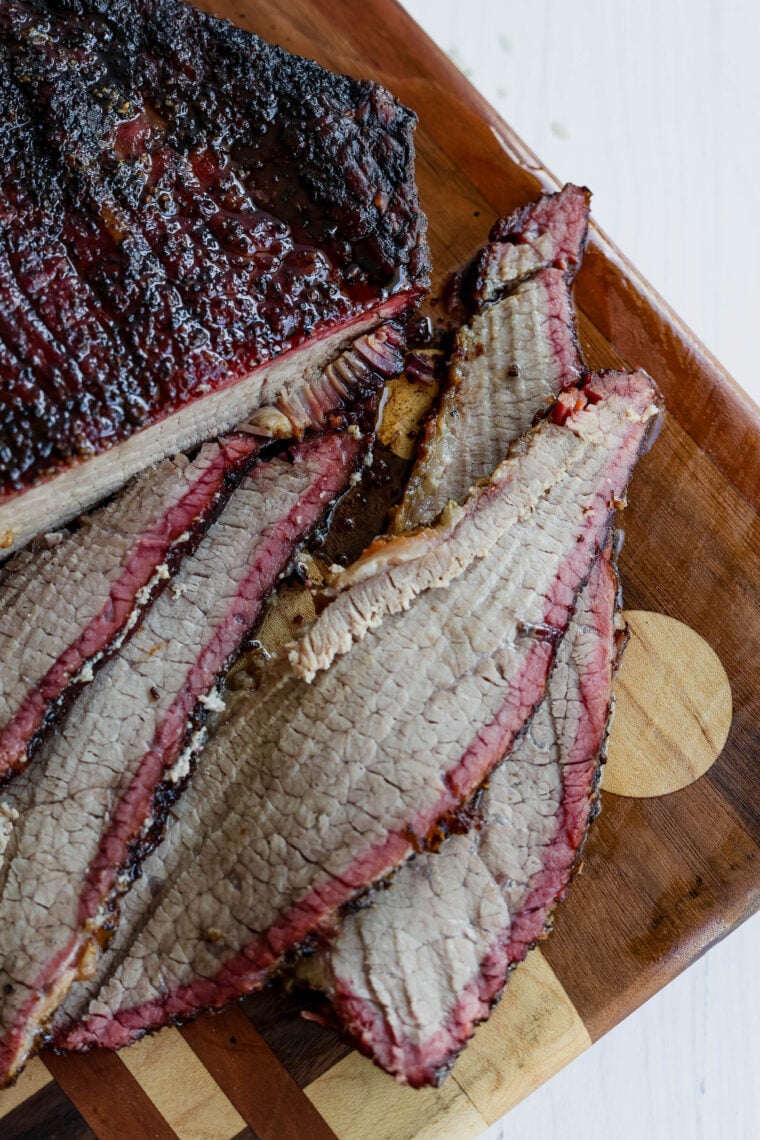 Sliced smoked brisket with a dark, flavorful crust and a juicy smoke ring—this tender meat is laid out on a wooden cutting board, ready to dig in.