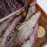 Sliced smoked brisket with a dark, flavorful crust and a juicy smoke ring—this tender meat is laid out on a wooden cutting board, ready to dig in.