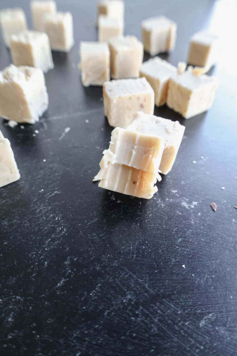 Beige cheese cubes are scattered on a dark, bumpy surface, kinda like white chocolate pieces. They look a bit crumbly and come in different sizes. The spotlights on this cute trio of cubes up front.