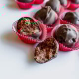 Chocolate truffles are chilling in red paper cups on a white background. Ones cracked open, showing off its rich buttercream middle. Theyre all wrapped up in silky dark chocolate and look super tempting!.