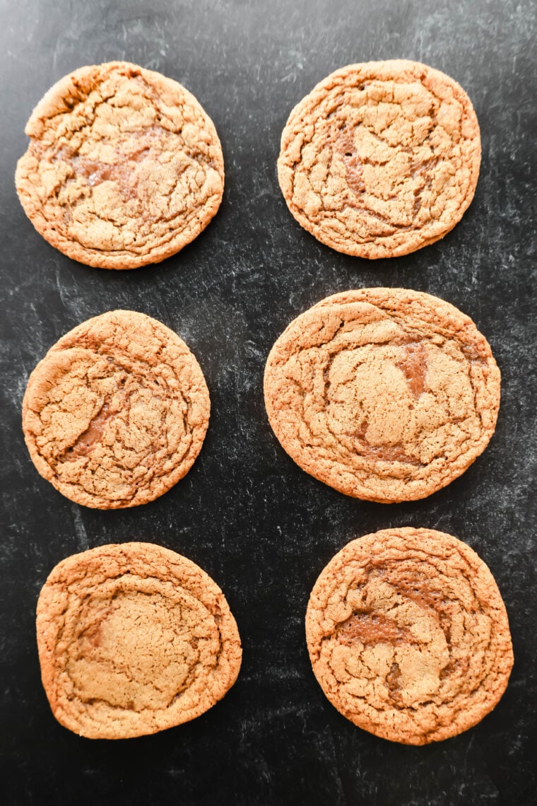 Six chewy chocolate chip cookies are lined up in two neat stacks of three on a dark, textured background. Their tops have that perfect crackle thing going on!.