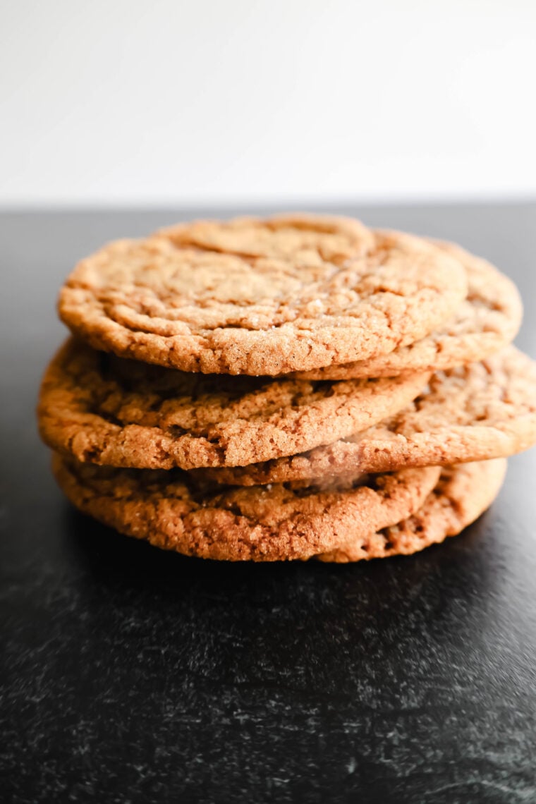 Three homemade molasses cookies are piled up on a dark surface, showing off their golden-brown, crispy goodness. With the background all blurred out, these soft and chewy treats totally steal the spotlight!.