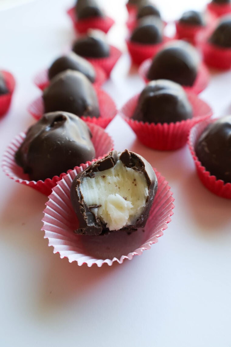 Imagine chocolate truffles lounging in red paper cups. One upfront has a bite taken out, showing off its creamy peppermint buttercream center. In the background, more truffles are chilling slightly out of focus. These would be awesome for your next candy-making adventure!.