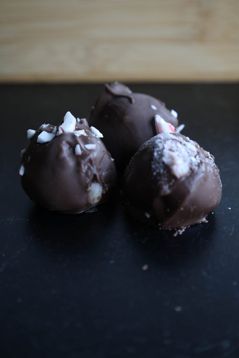 Three chocolate truffles chill on a dark surface, topped with crushed peppermint candy. The airs filled with the sweet scent of peppermint buttercream, and theres a wooden background setting off this tasty scene.