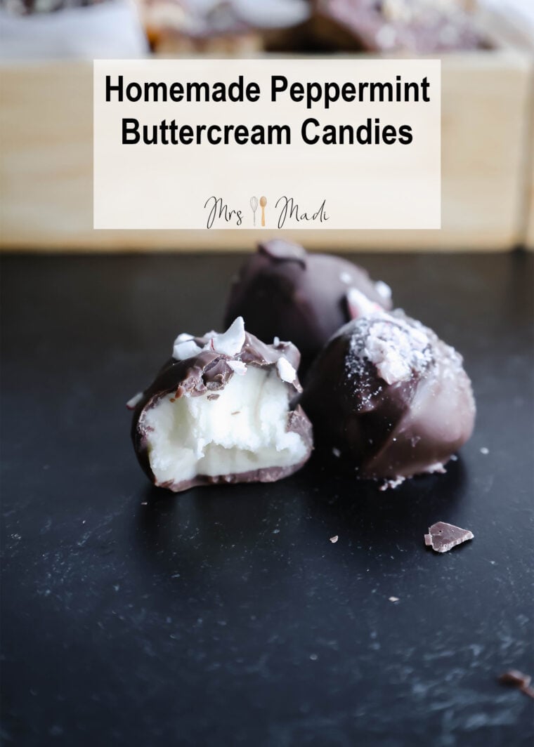 Check out these two chocolate-covered peppermint buttercream candies! Ones got a bite taken out, showing its yummy white filling. In the back, theres a wooden tray loaded with more goodies. A sign above says “Homemade Peppermint Buttercream Candies,” just begging you to give this tasty treat a try!.