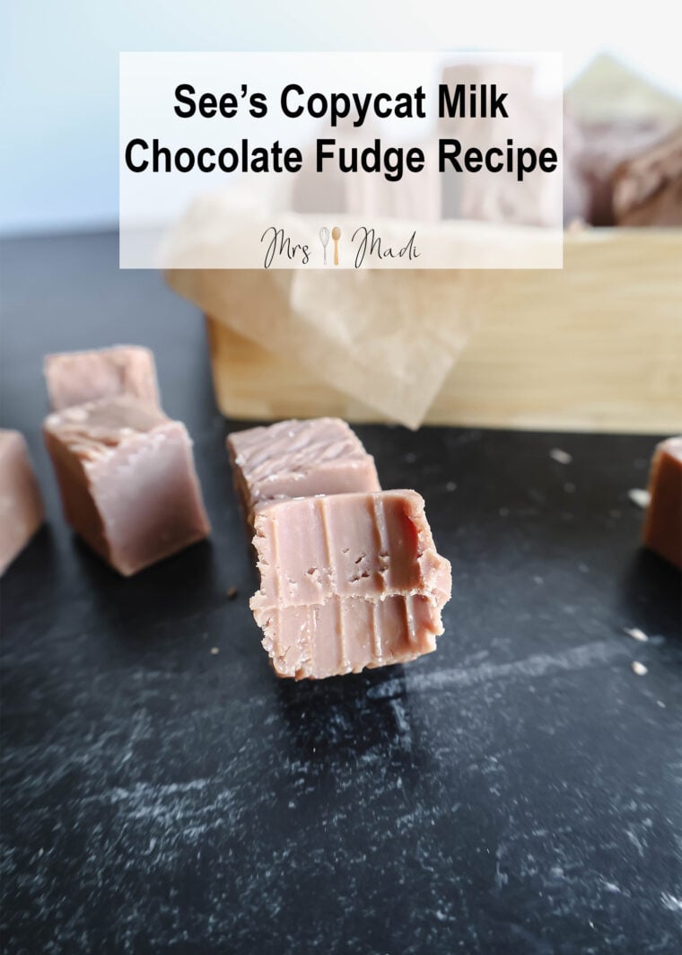 A close-up shot of tasty See’s fudge bits sitting on a dark table. In the back, theres a wooden box filled with even more fudge goodness. Up top, it says See’s Style Milk Chocolate Fudge Recipe.