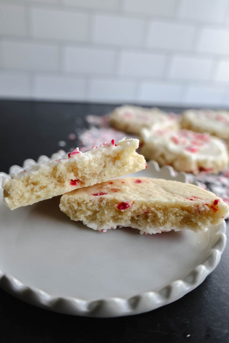 This shot zooms in on a cracked sugar cookie topped with white icing and red sprinkles, setting the festive mood. In the blurry background, there are more cookies with the same vibe on a dark surface.