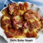 A plate of golden, crispy smashed potatoes with garlic butter on top, served on a white dish with a blue cloth in the background. At the bottom, it says: Garlic Butter Smash Potato Recipe.