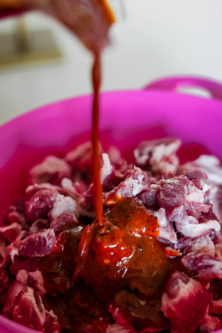 Here’s a close-up shot of raw diced meat in a pink bowl, with some yummy red marinade getting poured on top—just right for making a tasty al pastor salad!.