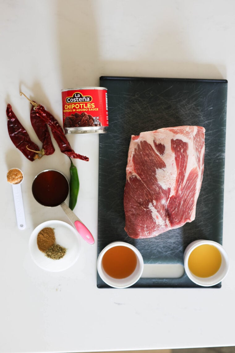 There’s a big hunk of raw beef on a black cutting board, surrounded by dried chilies, a can of chipotles, a green chili, some brown sugar, spices in a white bowl (perfect for making an al pastor salad), plus two little bowls of golden sauce.