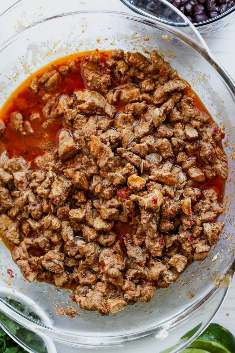 A glass bowl packed with juicy, seasoned ground beef tossed in a tasty red sauce—just right for an al pastor salad. You can see the spices and bits of onion, and it looks seriously delicious from above!.