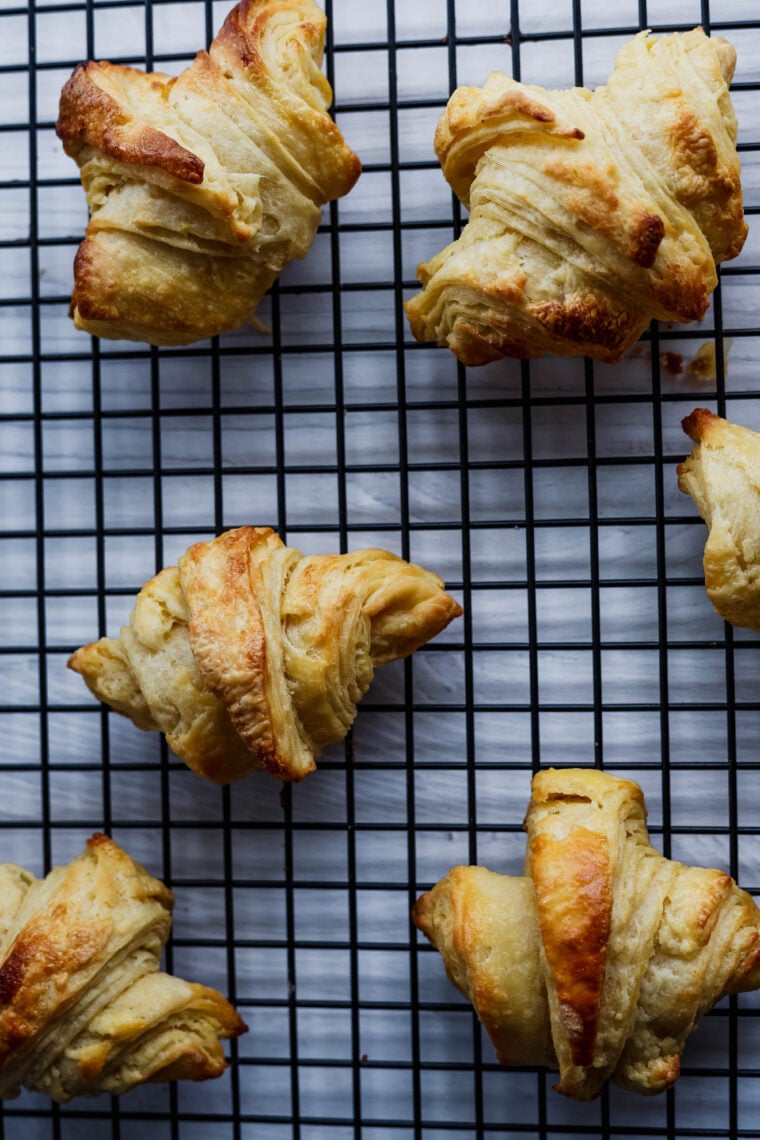 Freshly baked, golden brown croissants cooling on a black wire rack—top view, white background. Looking so good!.