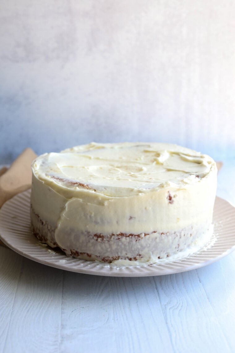 A round cake with white frosting sits on a plate, chilling on a light wood table with a simple background.