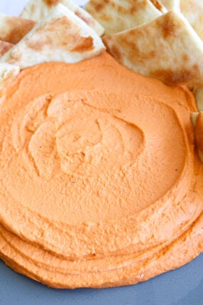 A plate covered in bright orange whipped feta dip, surrounded by plenty of pita bread for dipping.