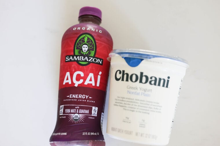 A bottle of Sambazon organic açaí energy juice and some Chobani nonfat plain Greek yogurt are sitting side by side on a white surface—ready to be whipped up into a tasty, refreshing acai bowl.