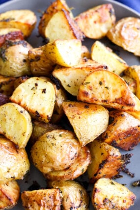Crispy, golden roasted potato wedges with a sprinkle of herbs, all served up on a gray plate.