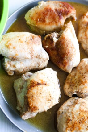 A few pieces of cooked, seasoned chicken are on a grey plate—some are nicely browned, others a bit lighter, all hanging out in a little bit of juice.