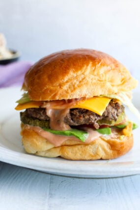 A mouthwatering cheeseburger loaded with melty cheese, fresh lettuce, and tasty sauce on a soft golden bun, all served up on a white plate.