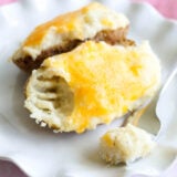 A fluffy baked potato split open, loaded with gooey melted cheddar, with a bite already taken and some cheesy goodness on a fork—all on a plain white plate.