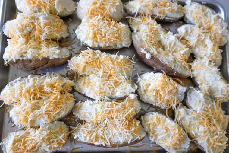 Potato halves on a baking sheet, loaded up with a creamy mix and a pile of shredded cheese—just waiting to hit the oven!.