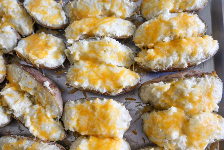 Twice-baked potato halves stuffed with creamy mashed potatoes and melty cheddar cheese, all cozied up together on a baking tray.