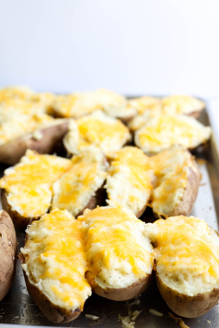 A tray of twice-baked potatoes is sitting on a metal baking sheet—each potato half is stuffed with creamy mashed filling and topped with gooey melted cheese.
