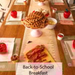 A table’s ready for a back-to-school breakfast—there’s waffles, bacon, fruit, and cute apple-shaped containers on placemats that look like notebook paper. There’s even a sign that says Back-to-School Breakfast Ideas & Recipes.