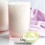 A bubbly coconut lime spritz in a pink glass sits next to a sliced lime on a bright surface, with a lavender cloth behind it. Text: Easy Coconut Lime Spritz Recipe.