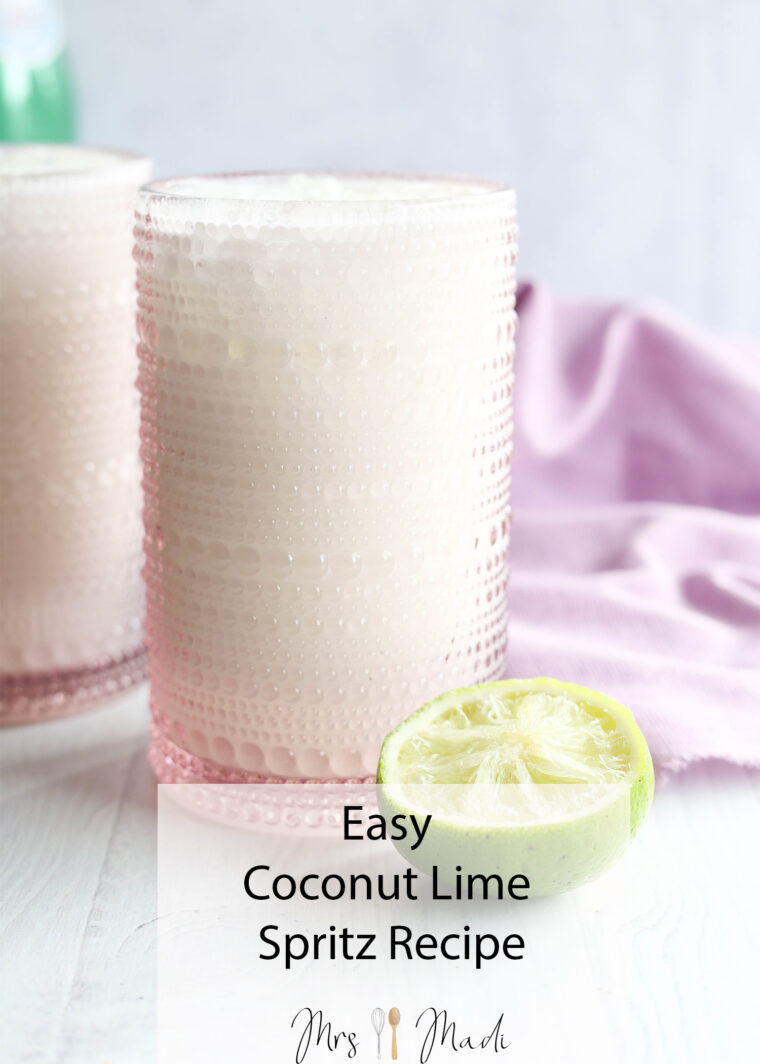 A bubbly coconut lime spritz in a pink glass sits next to a sliced lime on a bright surface, with a lavender cloth behind it. Text: Easy Coconut Lime Spritz Recipe.