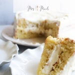 A piece of honey lemon olive oil cake with creamy frosting is on a white plate, right in front of the whole cake. The text up top says: Simple Honey Lemon Olive Oil Cake Recipe.