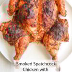 A juicy spatchcock chicken, roasted till the skin’s crispy and loaded with herbs, sits ready on a white plate. Smoked Spatchcock Chicken with Lemon & Herbs—yum!.