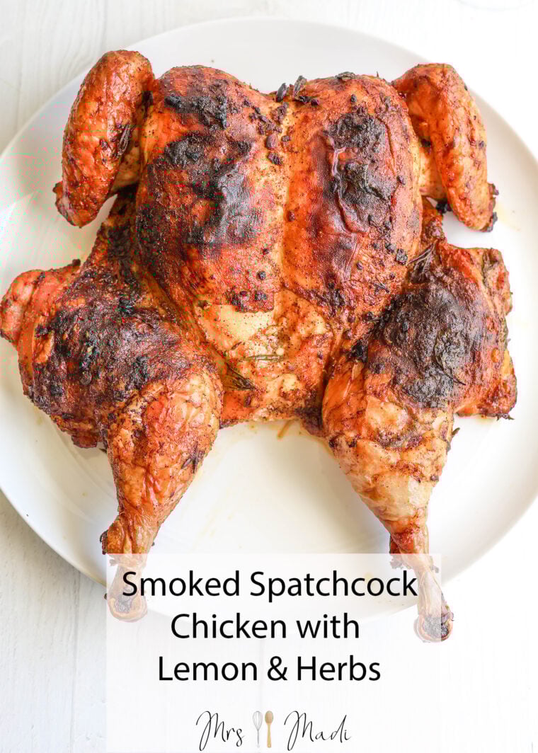 A juicy spatchcock chicken, roasted till the skin’s crispy and loaded with herbs, sits ready on a white plate. Smoked Spatchcock Chicken with Lemon & Herbs—yum!.
