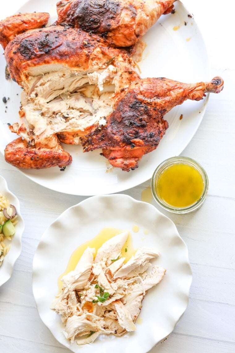 A juicy, roasted spatchcock chicken—already partly carved—sits on a big plate with a little jar of yellow sauce. Nearby, a smaller plate shows off chicken slices topped with sauce and fresh herbs.