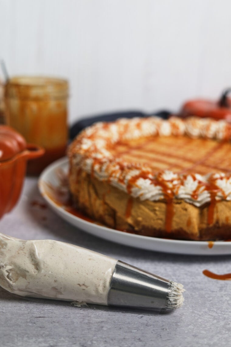 Cheesecake topped with cinnamon whipped cream and caramel, piping bag up front, caramel sauce jars in the back.