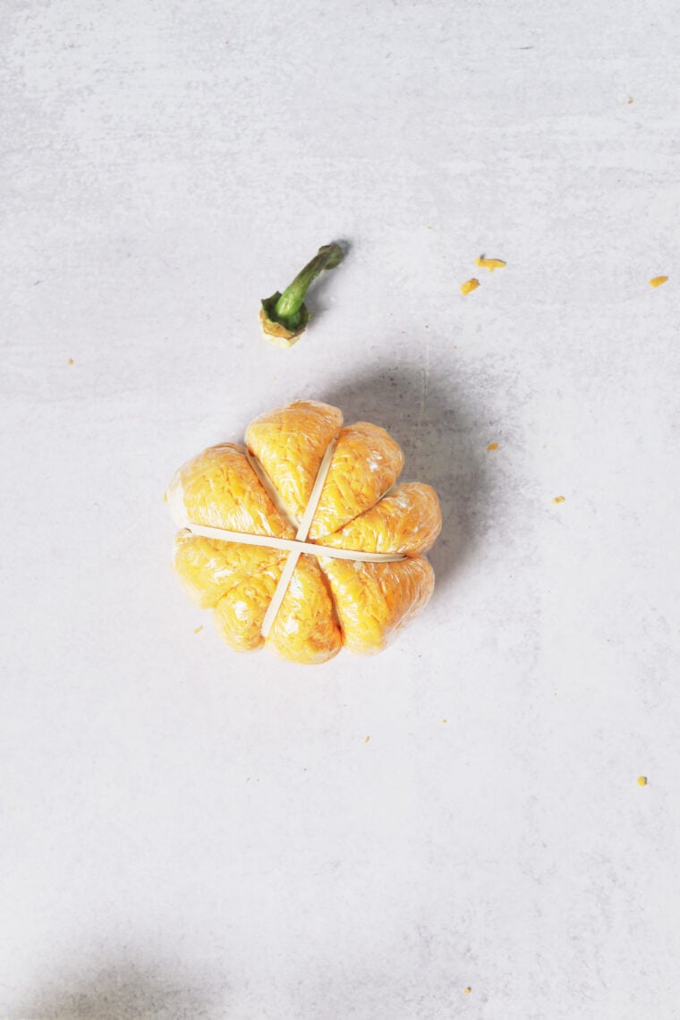Orange slices are laid out like a pumpkin cheeseball on a light table, with a green stem on top for that pumpkin vibe.