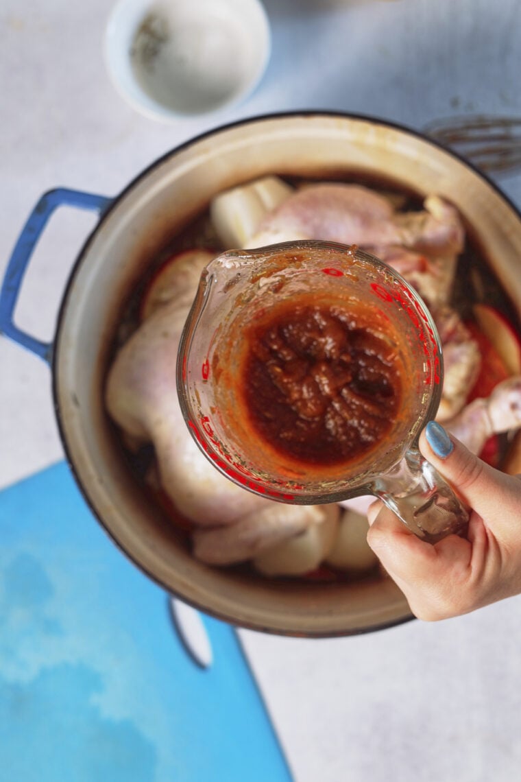 Pouring marinade into a pot with raw chicken and onions, with a cutting board and bowl close by for the tasty prep.