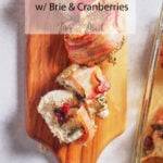 Sliced bacon-wrapped chicken stuffed with brie and cranberries on a wood board, text says “Bacon-Wrapped Stuffed Chicken w/ Brie & Cranberries Mrs. Made.”.