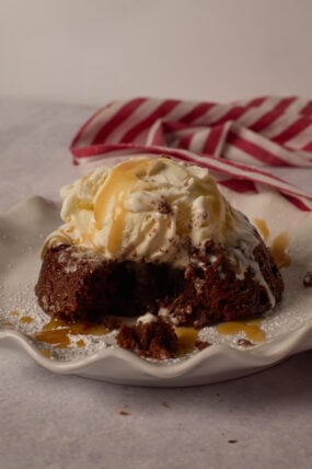 Chocolate lava cake with vanilla ice cream and caramel sauce on a white plate, next to a red and white striped cloth.