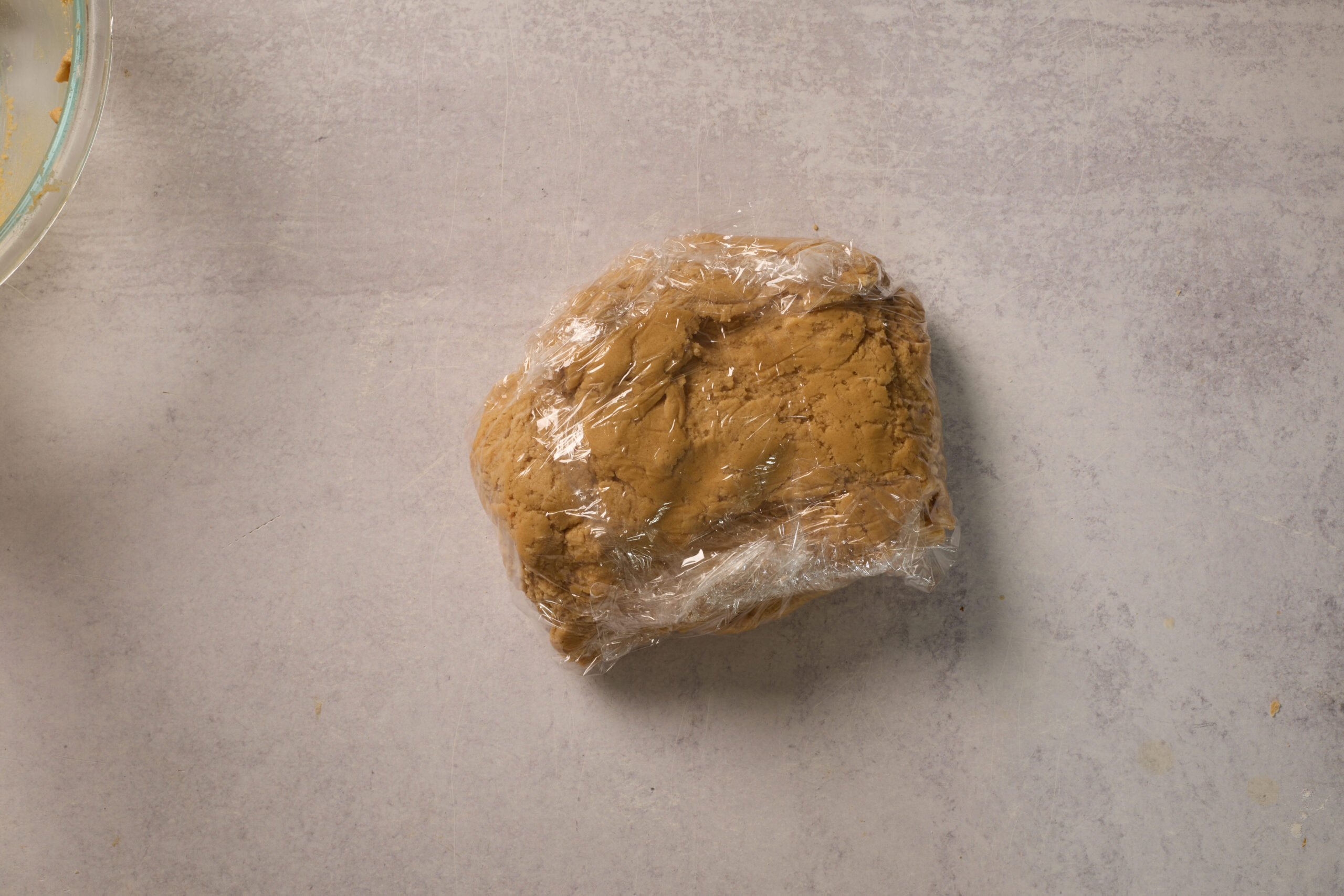 There's a ball of dough snug in plastic wrap chilling on a light countertop.